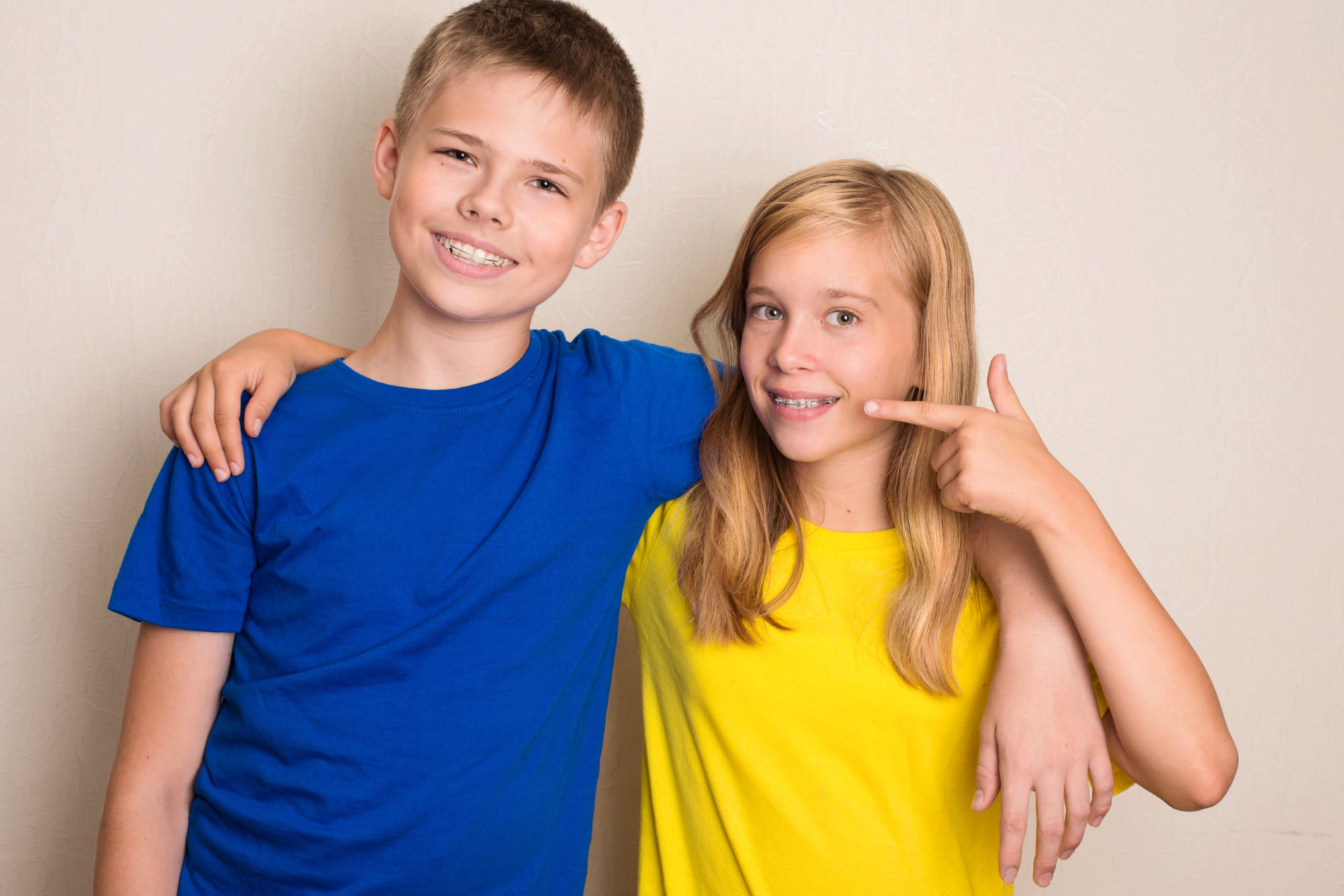 Two children, a boy in a blue shirt and a girl in a yellow shirt, smiling and showcasing their braces, representing orthodontic care for kids at Pechersky Orthodontics in Pittsburgh.