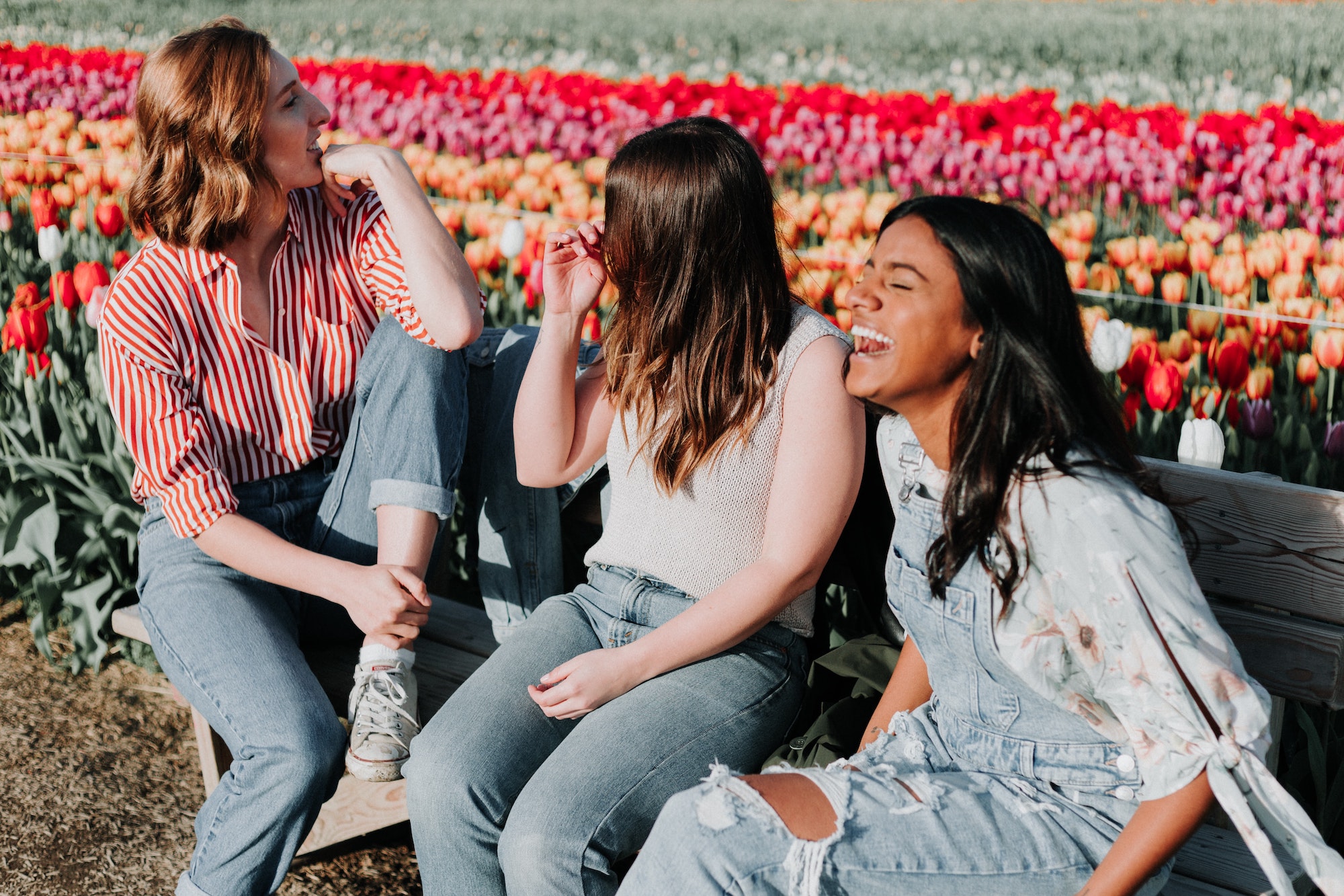 Three young women laughing and enjoying time together in a vibrant tulip field, highlighting the joy of orthodontic treatment experiences at Pechersky Orthodontics, a leading Pittsburgh orthodontist.